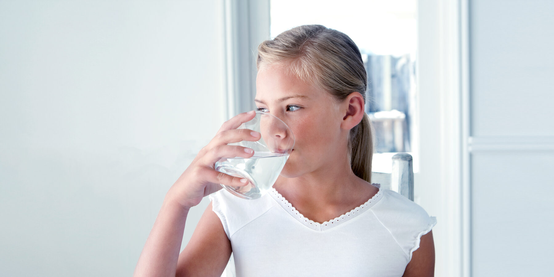 Woman drinking a glass of water in a bright kitchen